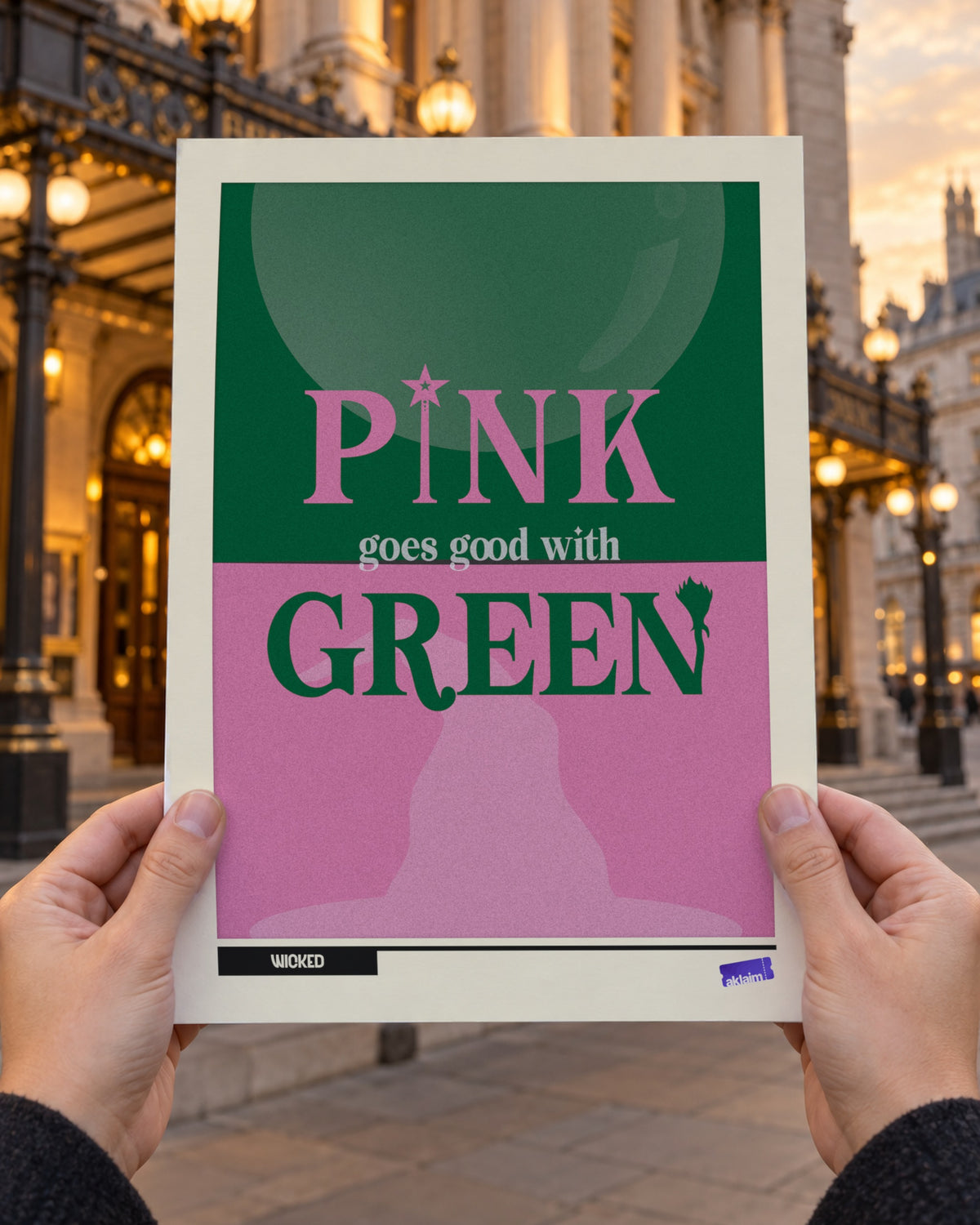 Pink Goes Good With Green Wicked poster held up in two hands outside a London theatre at golden hour