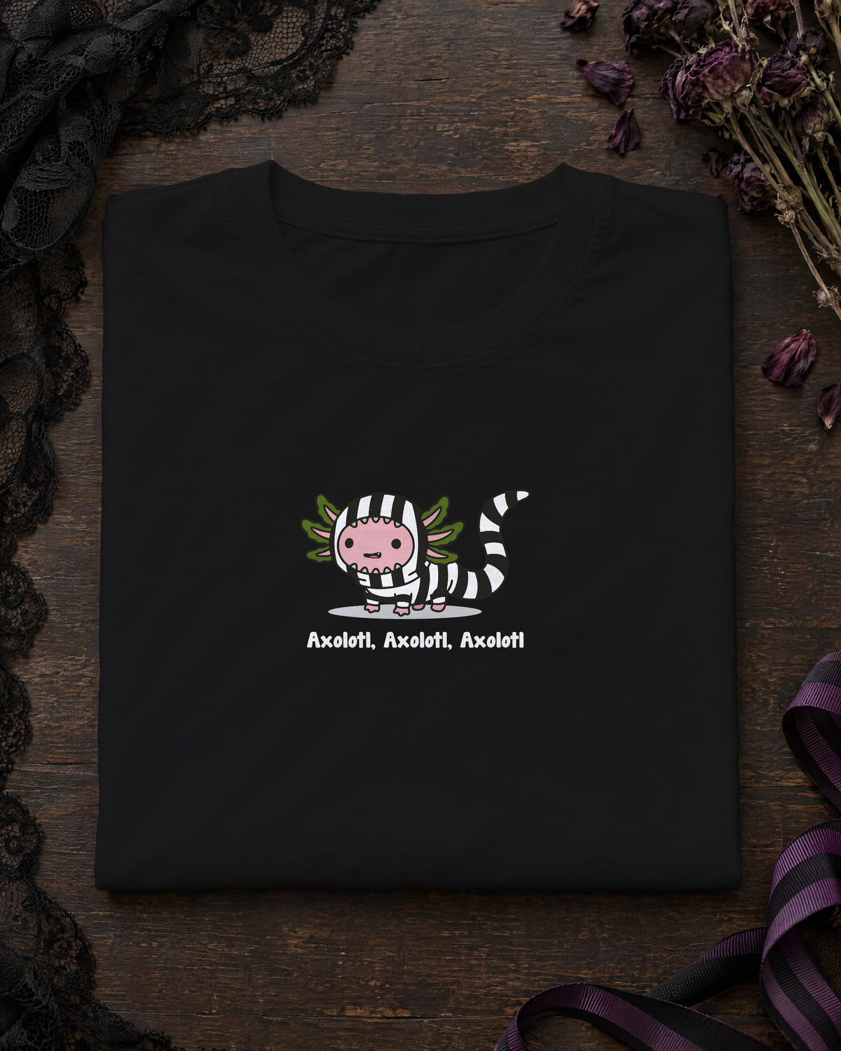 Axolotl Beetlejuice t-shirt in Black, folded on a dark table with a lace veil and dried flowers