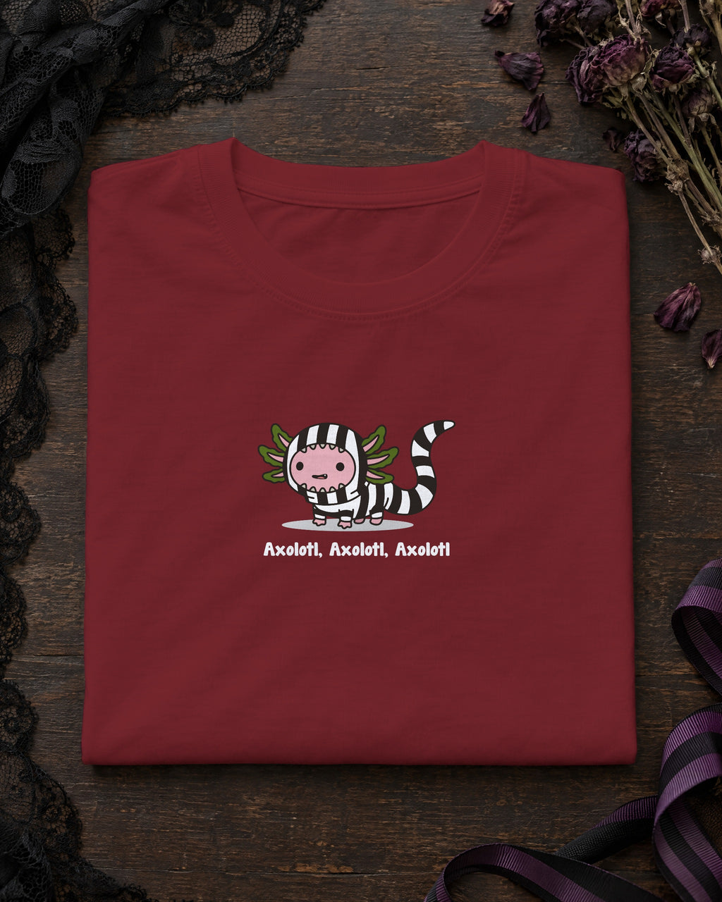 Axolotl Beetlejuice t-shirt in Burgundy, folded on a dark table with a lace veil and dried flowers