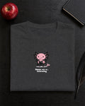 Humans Are So Interesting t-shirt in Dark Heather Grey, folded on a black desk with an apple, a notebook and a quill