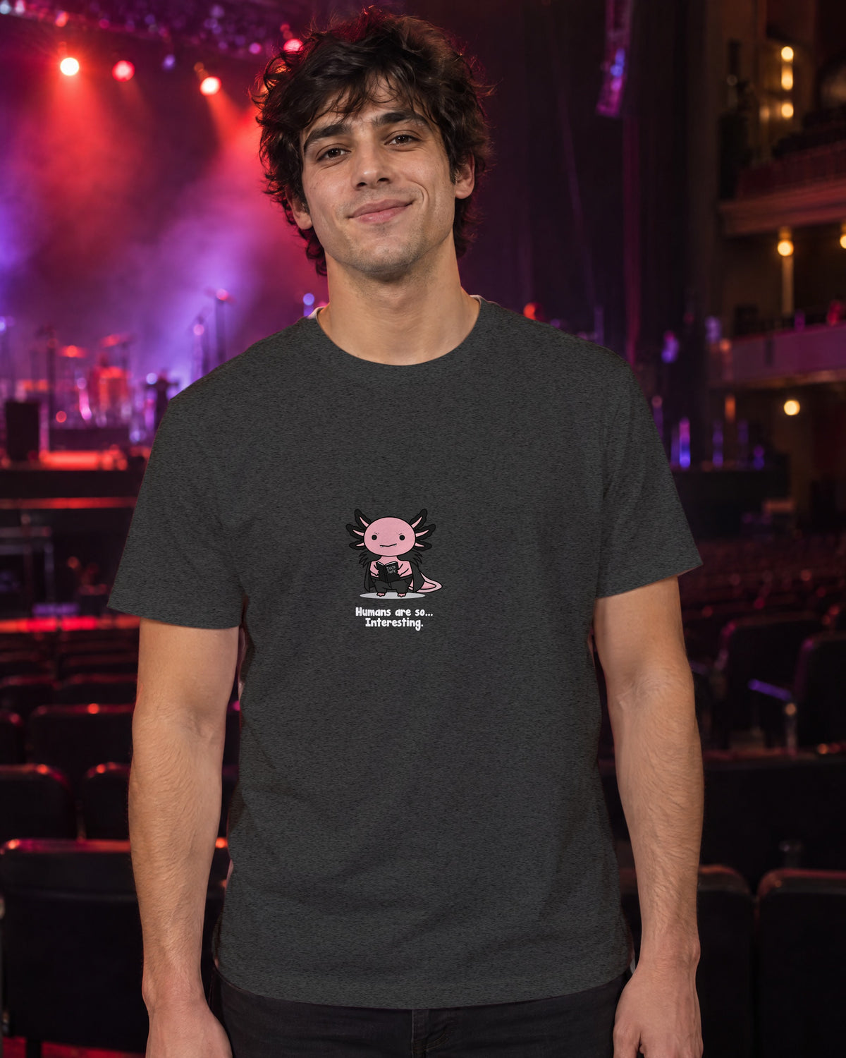 Humans Are So Interesting t-shirt in Dark Heather Grey, worn in a theatre under red and violet stage light