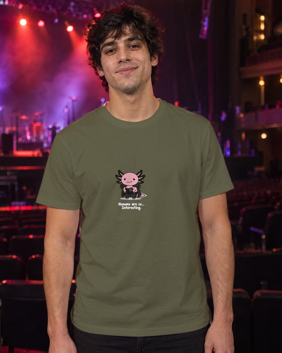 Humans Are So Interesting t-shirt in Khaki, worn in a theatre under red and violet stage light