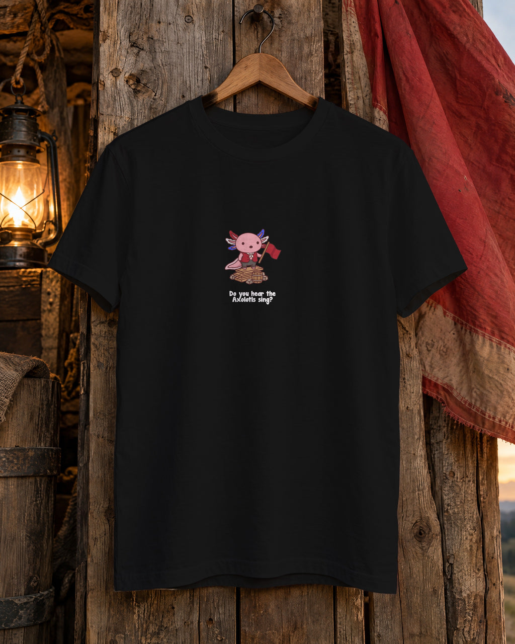 Do You Hear the Axolotls Sing t-shirt in Black on a hanger against barricade planks with a red flag