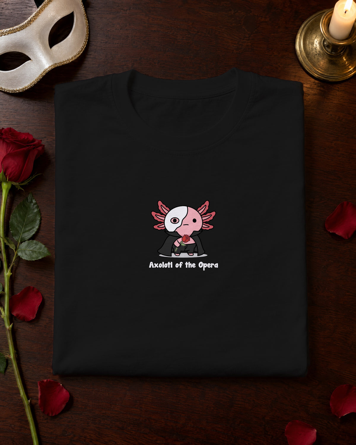 Axolotl of the Opera t-shirt in Black, folded on a dressing table with a mask and a red rose