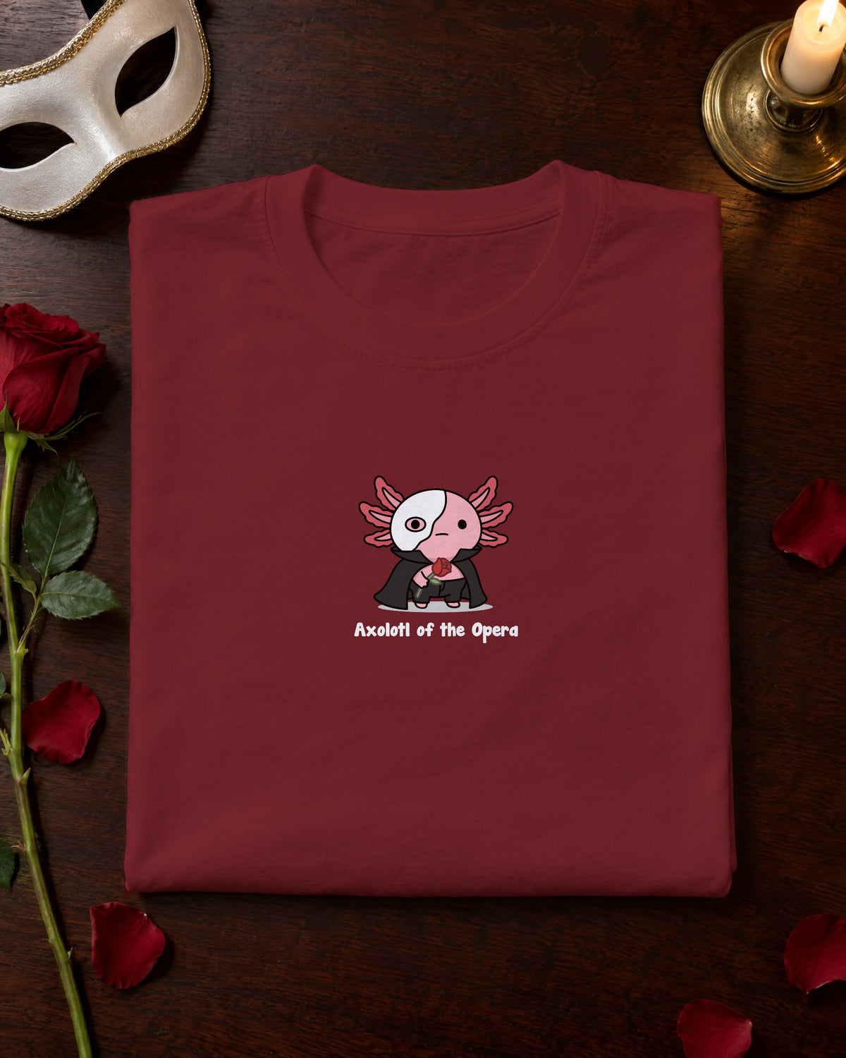 Axolotl of the Opera t-shirt in Burgundy, folded on a dressing table with a mask and a red rose